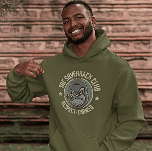 A younger man wearing an olive green hooded sweatshirt with a logo of a silverback gorilla head smoking a cigar and the words The Silverback Club and Respect.Earned surrounding it.