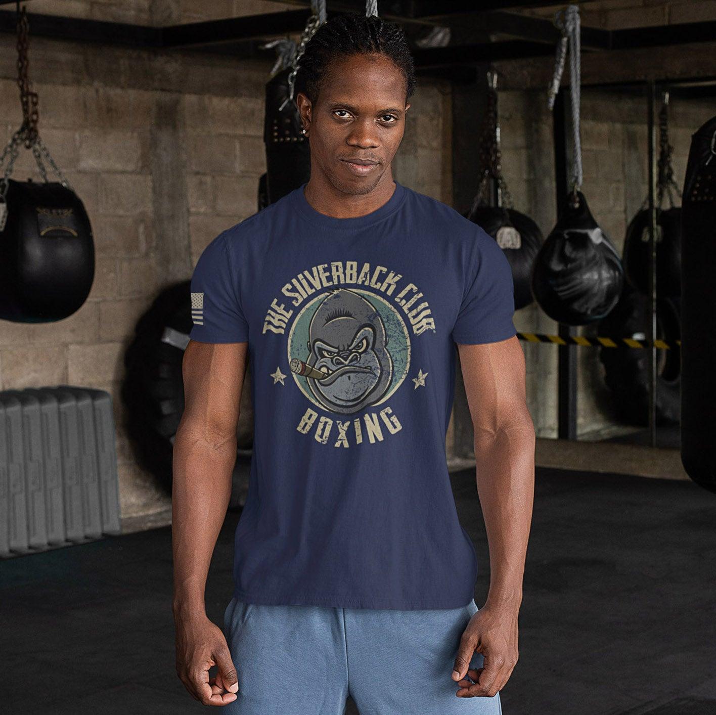 A man wearing a blue t-shirt with The Silverback Club logo consisting of a gorilla face smoking a cigar and the words "Boxing" underneath.