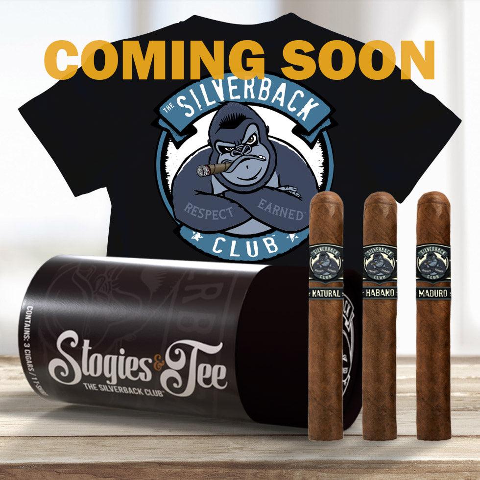 An image of a black t-shirt with The Silverback Club logo of a gorilla smokikng a cigar and folding his arms. The words "Respect" and "Earned" are on its forearms. A brown cylinder tube package to hold the t-shirt and cigars with the words "Stogies & Tee". Three cigars with The Silverback Club logo on them and the words "Natural", "Habano", and "Maduro" on them. "Coming Soon" is at the top of the image.