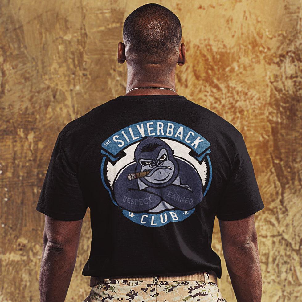 A military man with a black t-shirt standing backwards showing The SIlverback Club logo of a gorilla smoking a cigar and folding its arms. The words "Respect" and "Earned" are on its forearms.