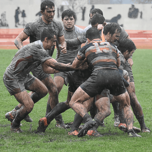 Men playing rugby and are in a scrum, muddy, and fighting for the ball.