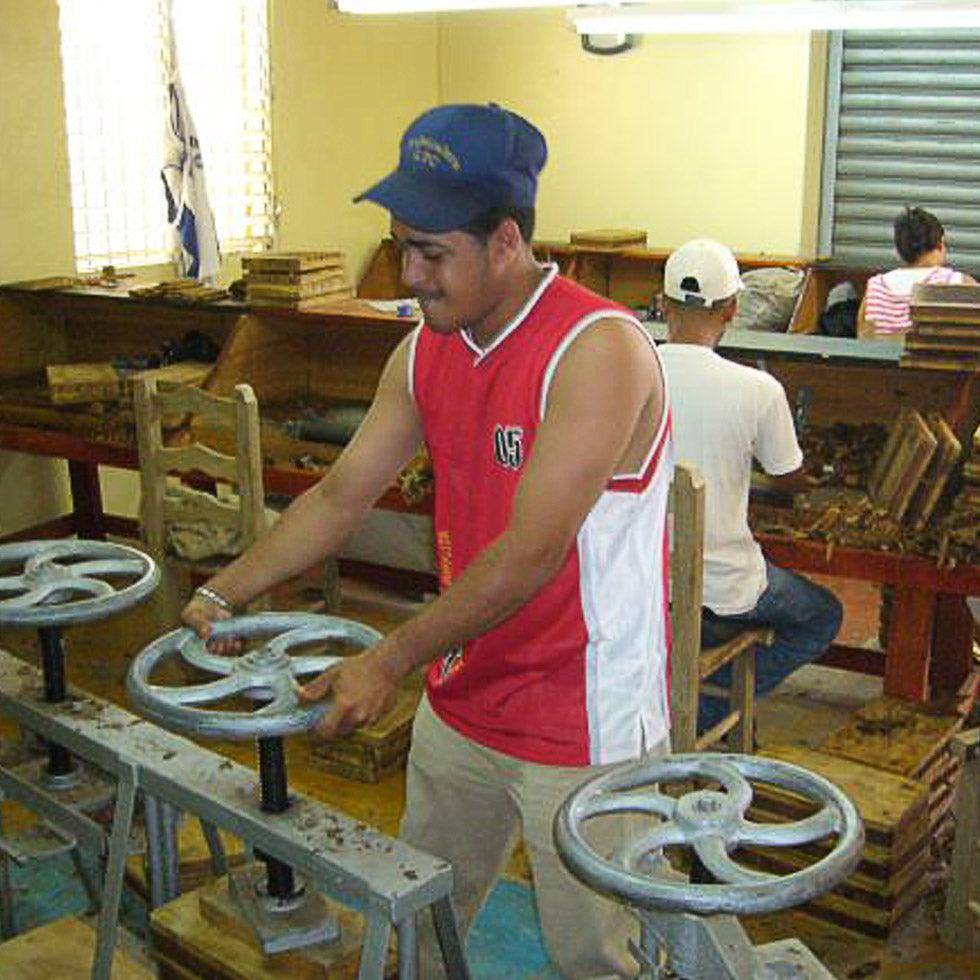 A man using a cigar mold press to produce cigars.